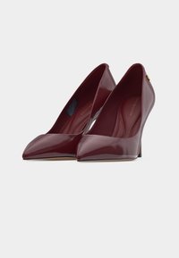 Ζευγάρι γυναικείων κόκκινων μυτερών ψηλοτ άκουνων παπουτσιών με στιλέτο τακούνια πάνω σε απλό φωτεινό φόντο.