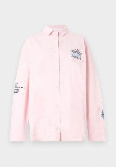 Ροζ ανοιχτό μακρυμάνικο πουκάμισο με κουμπιά, με κεντητό ήλιο και κύματα στην τσέπη στο στήθος και μικρό κείμενο και σχέδια σε κάθε μανίκι.
