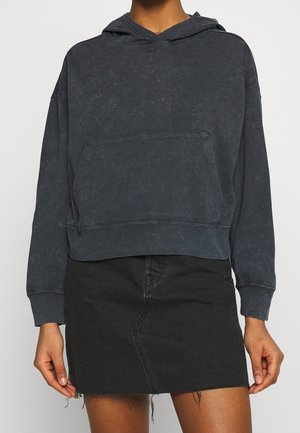 Persoon die een gewassen zwarte cropped hoodie met kangaroezak en een zwarte denim rok met rafelige zoom draagt.