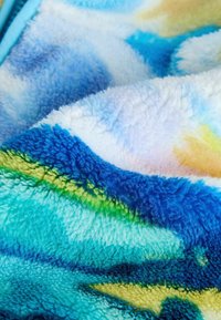 Couverture duveteuse présentant un motif de vagues colorées en bleu, vert et jaune ; texture douce avec une surface pelucheuse et moelleuse.