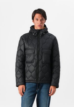 Schwarze, gesteppte Daunenjacke mit Kapuze, zwei Vorderaschen, Frontreißverschluss und glatter, glänzender Textur. Über Jeans getragen.