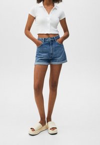 Pantalones cortos de denim con dobladillos enrollados, de cintura alta, combinados con una camiseta corta de canalé blanca y sandalias de plataforma beige.