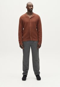 Pruun ribaga kardigan nööpidega, koos hallide pükstega. Komplektis on mugav lõige ja kindlad tekstuurid, mida täiendavad mustad kingad.