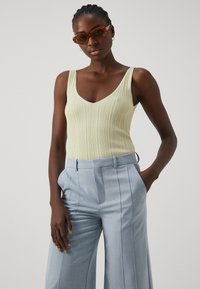 Lys gul ribbet tanktop med dyp V-hals, paret med høy midje lys blå vide bukser. Tilbehør med brune solbriller.
