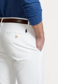 Białe spodnie bawełniane o slim fit, z tylną kieszenią, zapięciem na guzik oraz małym granatowym logo na prawej tylnej kieszeni.