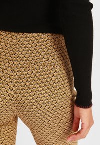 Haut noir à manches longues en tissu côtelé associé à un pantalon à motifs jaune et marron arborant un design floral et un détail contrastant en bas.
