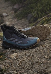 Zapatos de senderismo impermeables en negro y azul con superficie texturizada, suela de goma acanalada y puntera prominente. Presenta detalles reflectantes y un logotipo.