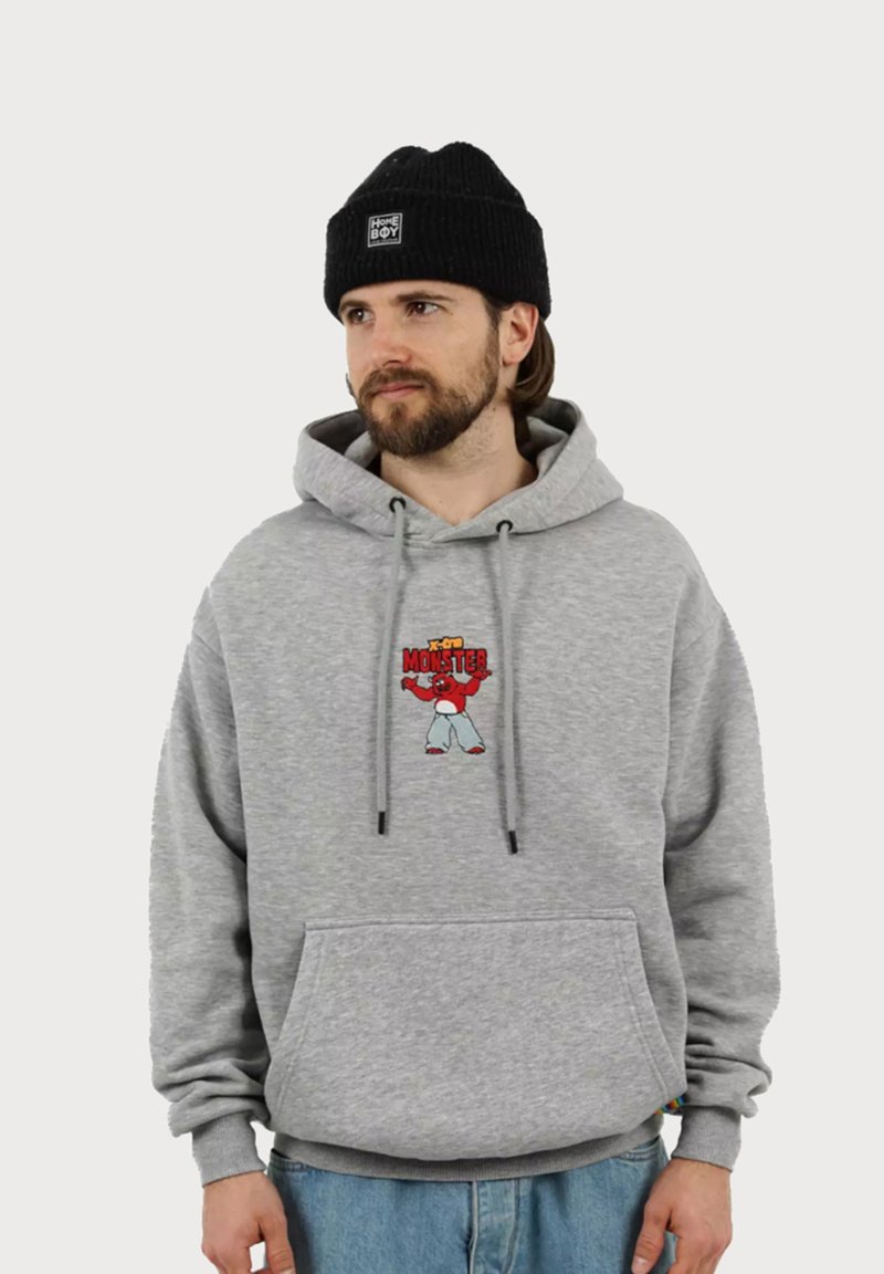 Felpa grigia con tasca frontale e cappuccio regolabile, caratterizzata da un design di un personaggio dei cartoni animati rosso sul petto. Berretto lavorato a maglia nero sulla testa.