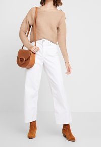 Beige ribstrikket sweater, hvide vidde benbukser og brune ruskind ankle boots. En brun læder crossbody taske med et rundt håndtag.