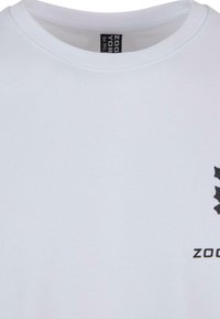 Hvid kortærmet t-shirt med rund hals og et sort grafisk design på venstre bryst, som viser teksten "ZOORYOR" samt et mønster.