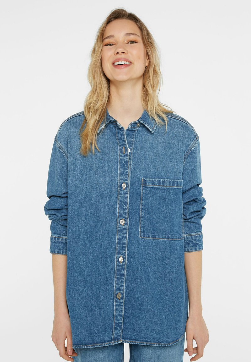 Denim shirt in blue with long sleeves, button front, single chest pocket, and a relaxed fit. Fabric has a textured finish.