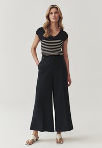 Marine wijde broek met twee voorknopjes, gecombineerd met een fitted zwart-wit gestreept shirt met korte mouwen. Textuurstof.