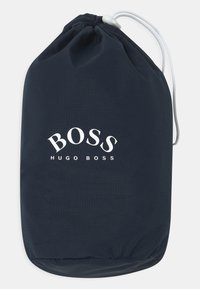 Bolsa de cordón azul marino hecha de material ligero con el logotipo "BOSS HUGO BOSS" en blanco, textura suave y fondo redondeado.