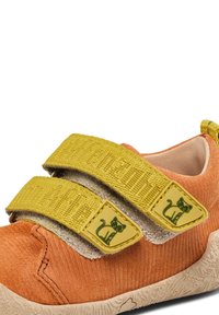 Oranje suede schoen met gele stoffen banden en kattenvormige accenten, evenals een gestructureerde beige rubberen zool.