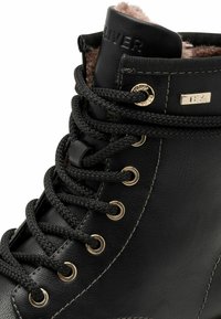 Bottine en cuir noir avec surface texturée, œillets en or et lacets noirs. Dotée d'une doublure en fausse fourrure en haut pour plus de chaleur.