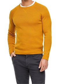 Senfgelbes Strickpullover mit langen Ärmeln, Rundhalsausschnitt und strukturiertem Stoff. Kombiniert mit dunkelgrauen Hosen, was einen lässigen Look zeigt.