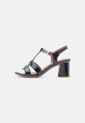 Black patent leather sandal with a T-strap design, open toe, and a block heel. Features adjustable ankle buckle and flat straps.