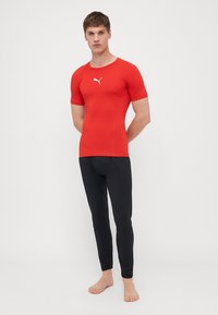 Rød treningstrøye med korte ermer og en hvit logo, kombinert med svarte tettsittende leggings, begge i glatt og elastisk stoff.