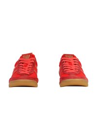Zapatillas rojas con parte superior de tela, detalles en ante texturizado, cordones planos y suela de goma. Presenta un logo dorado en la lengüeta y rayas laterales.