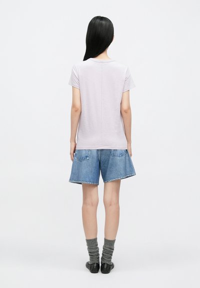 T-shirt de manga curta em lavanda clara com um corte descontraído, combinado com calções de ganga azuis ao estilo solto e com dois bolsos traseiros.