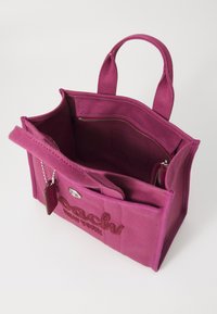 Pink canvas bag with dual handles, interior zip pocket, and embroidered logo detail on front. Open top reveals main compartment and pockets.