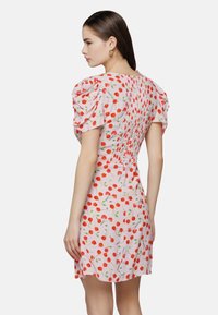 Kurzes pinkes Kleid mit Puffärmeln, das mit einem roten Kirschmuster versehen ist. Elastisches Smocking am Rücken sorgt für Textur und Form.