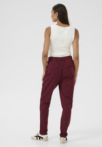 Pantalons bordeaux à taille élastique avec poches latérales, associés à un haut sans manches blanc et des baskets blanches avec des accents noirs.