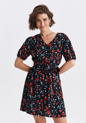 Czarna sukienka w kwiaty z krótkimi bufkami, ozdobiona czerwonymi i niebieskimi kwiatami oraz białymi kropkami, z przewężoną talią i szczegółem wiązania.