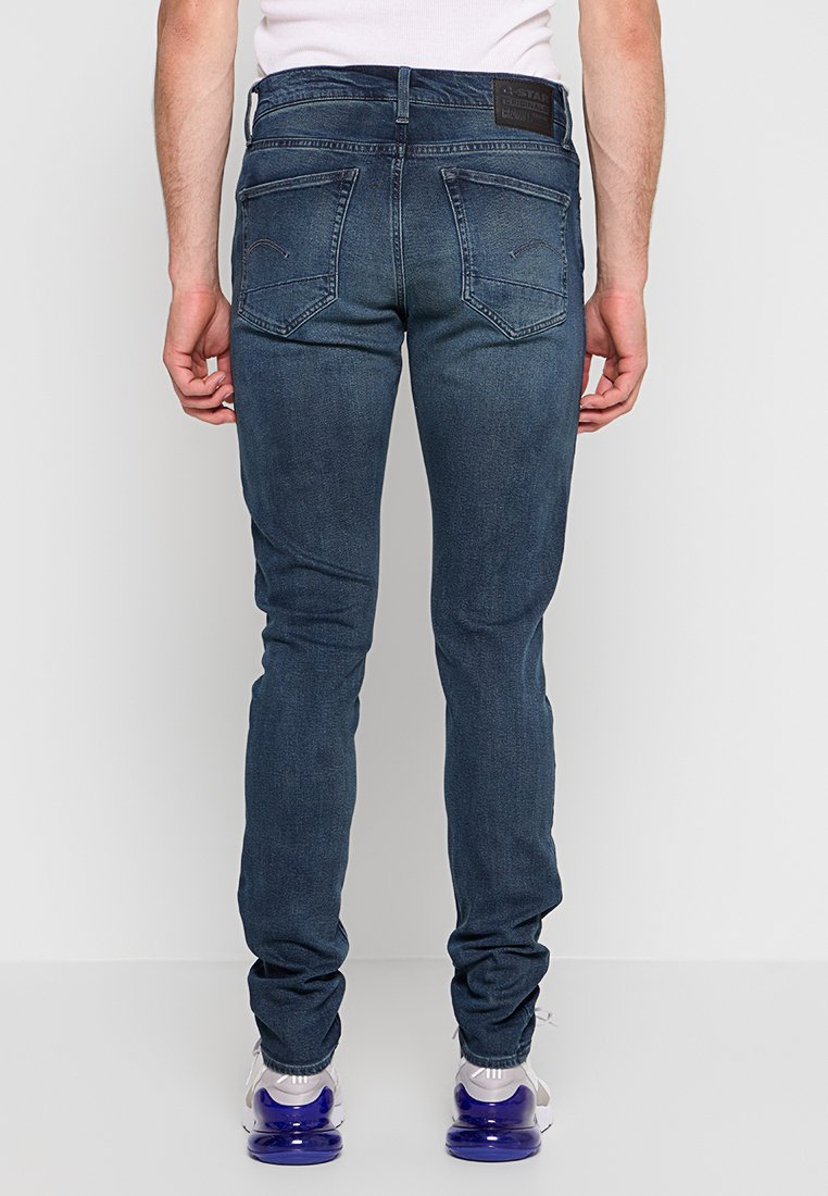 Jean en denim bleu foncé à coupe slim, avec deux poches arrière, des coutures discrètes et une étiquette en cuir à la taille.