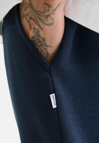 Tamno plava pamučna majica s V-izrezom, koja sadrži vidljivu bijelu etiketu s natpisom "JACK & JONES" na rubu i teksturirane detalje tkanine.