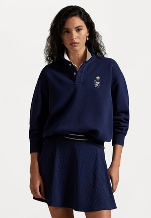 Sweatshirt azul-marinho com colarinho branco e logótipo bordado, combinado com uma saia texturizada a condizer. O conjunto apresenta um corte descontraído e punhos canelados.