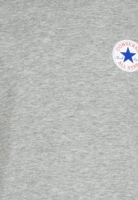 Grå sweatshirt i ett bomullsblandat tyg, med rund halsringning och en cirkulär logotyp med en blå stjärna och röd kant.