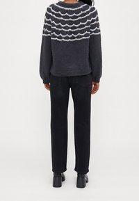 Szary sweter z dzianiny z białym wzorem fal na karczku, w połączeniu z czarnymi spodniami o prostym kroju i czarnymi botkami za kostkę.