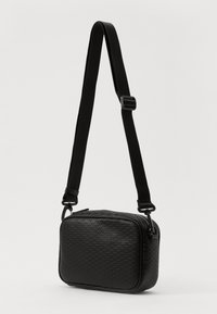 Borsa a tracolla nera con superficie testurizzata, forma rettangolare, chiusura con zip e tracolla regolabile. Presenta dettagli hardware lisci.