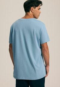 Jasnoniebieska bawełniana koszulka z krótkim rękawem, luźny krój i okrągły dekolt. Gładka faktura z prostym wzorem, bez widocznych wzorów.