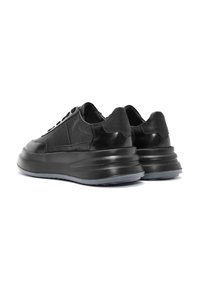 Zapatillas negras de cuero con paneles texturizados y lisos, punta redonda, parte delantera con cordones y suela de goma gruesa que se estrecha en el talón.