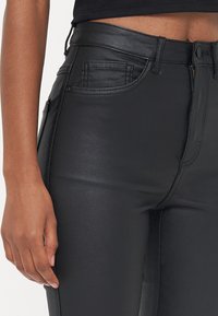 Zwarte faux leren high-waisted broek met vijfzakkenontwerp, voorzien van een gladde textuur en een rits aan de voorkant. Perfecte pasvorm en strakke uitstraling.