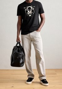 Černé bavlněné tričko s grafikou tygra, světle šedé džíny, černé tenisky s bílou podrážkou a černá taška přes rameno.