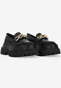 Mocassini neri con suola in gomma testurizzata, in pelle. Una catena dorata adorna la parte anteriore per un tocco di dettaglio in più.