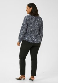 Marinebluse mit weißem abstraktem Druck, langen Ärmeln und lockerer Passform; kombiniert mit schwarzen Skinny-Jeans und schwarzen High Heels.