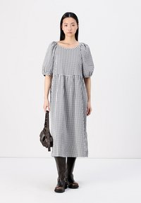 Vestido checkered preto e branco com mangas bufantes, corte solto e costura na cintura. Combinado com botas de couro castanho até ao joelho e uma mala de ombro.