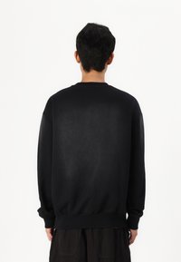 Black sweatshirt made of soft fabric, featuring a classic crew neckline, long sleeves, and a relaxed fit with ribbed cuffs and hem.