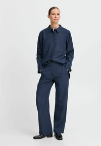 Ensemble de chemise et pantalon rayé bleu marine. La chemise a un col, une fermeture à boutons et deux poches poitrine. Les pantalons sont de coupe droite.