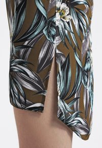 Hnědé květinové šortky se šlicem na boku, se vzorem velkých tyrkysových listů a bílých květin, vyrobené z lehkého materiálu.