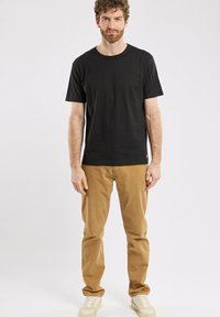 T-shirt en coton noir avec un col rond, associé à un pantalon chino beige. Les détails notables incluent des baskets beige clair et un design simple.
