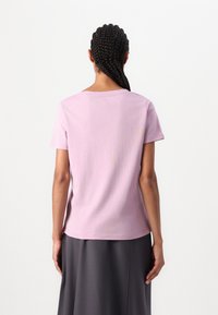 Ljusrosa t-shirt med korta ärmar, rund halsringning och avslappnad passform. En enkel design med en mjuk textur, kombinerad med en grå kjol.