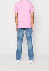 Růžové tričko s krátkým rukávem a kulatým výstřihem, kombinované se světle modrými džíny. Klasický střih, neformální styl, zobrazeno zezadu.