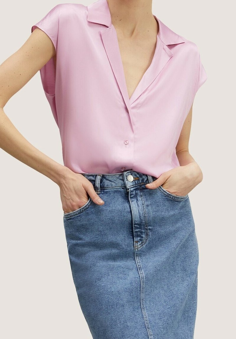 Blouse rose clair à manches courtes avec un col en V et des boutons, associée à une jupe en denim taille haute de teinte moyenne.