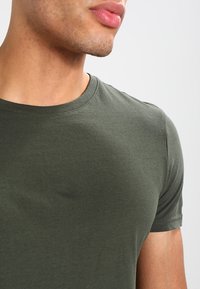 Olivengrøn crew neck t-shirt, lavet af blød bomuld, med korte ærmer og en glat tekstur med et enkelt, klassisk design.