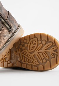 Bottine en métal bronze avec une fermeture éclair latérale et une semelle en caoutchouc texturée présentant un motif de feuilles et de fleurs.